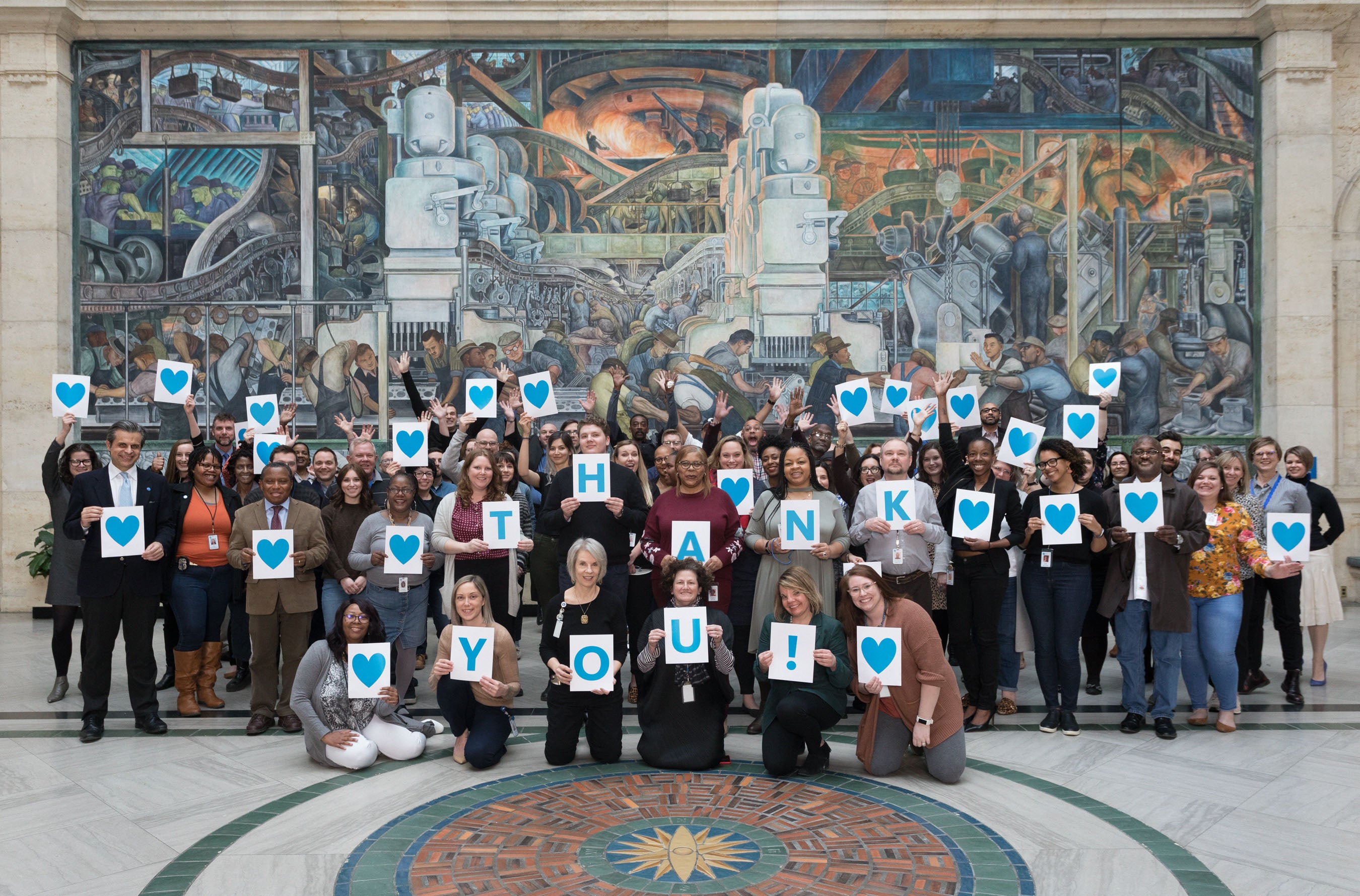The staff of the DIA pictured in Rivera Court holding signs that say "Thank You"